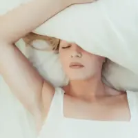 woman-lays-in-a-bed-with-a-pillow-over-her-head